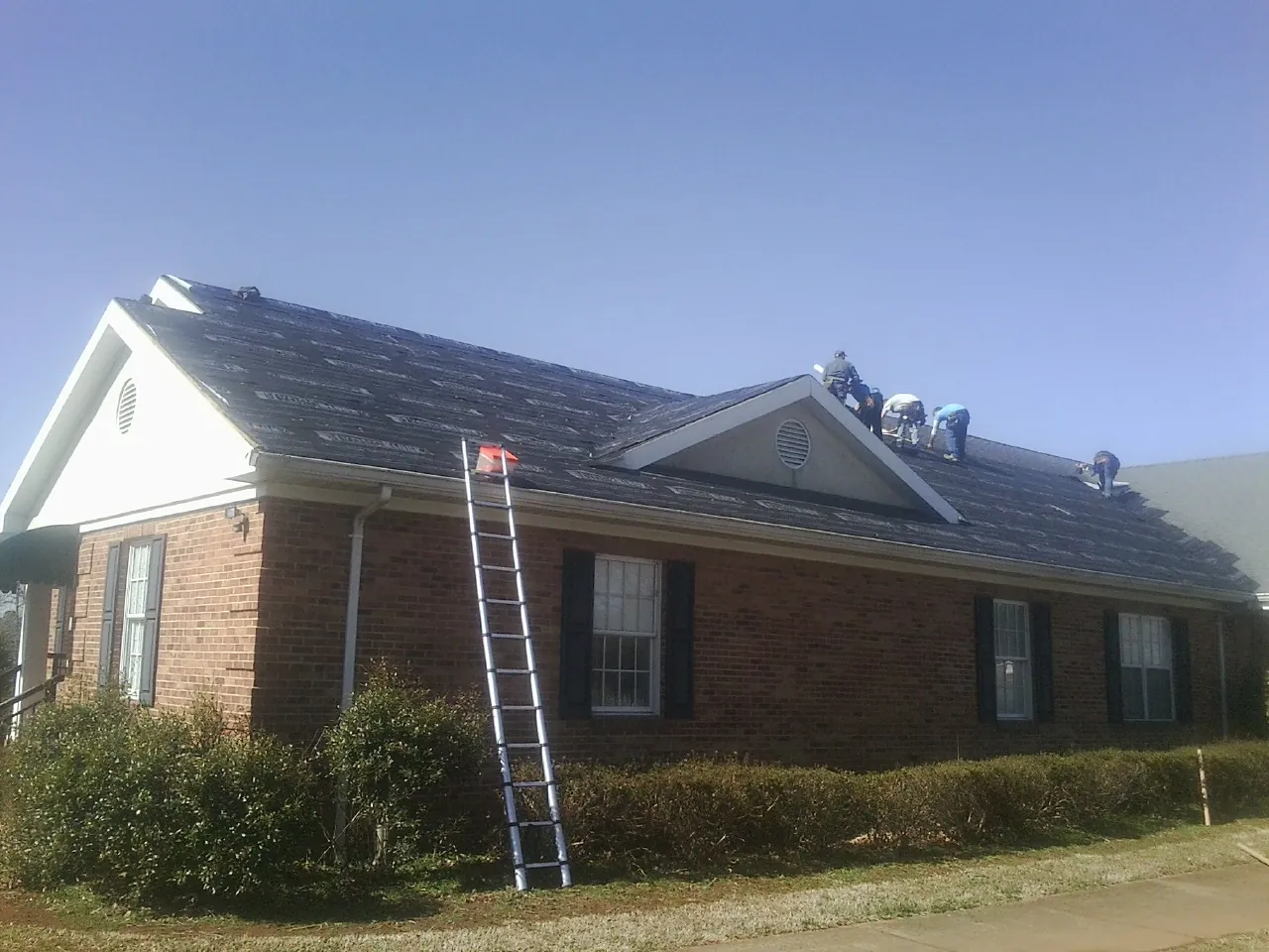 Crew tearing shingles off a brick ranch roof with a ladder set — Emergency Roof Repair work by our crew in Courtland