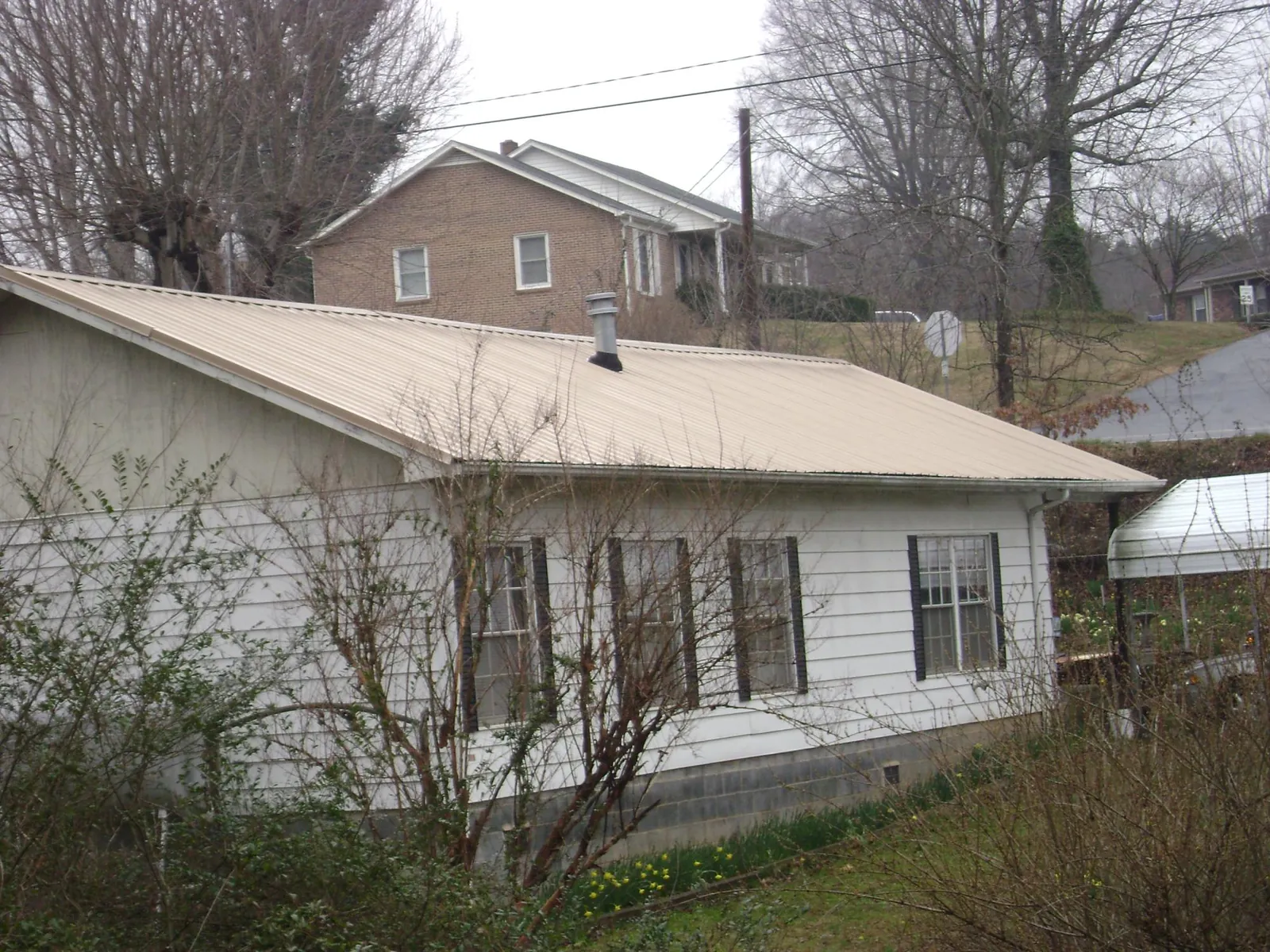 Tan metal roof on a white sided house set into a hillside — Commercial Roofing by Roofing Brothers in Courtland